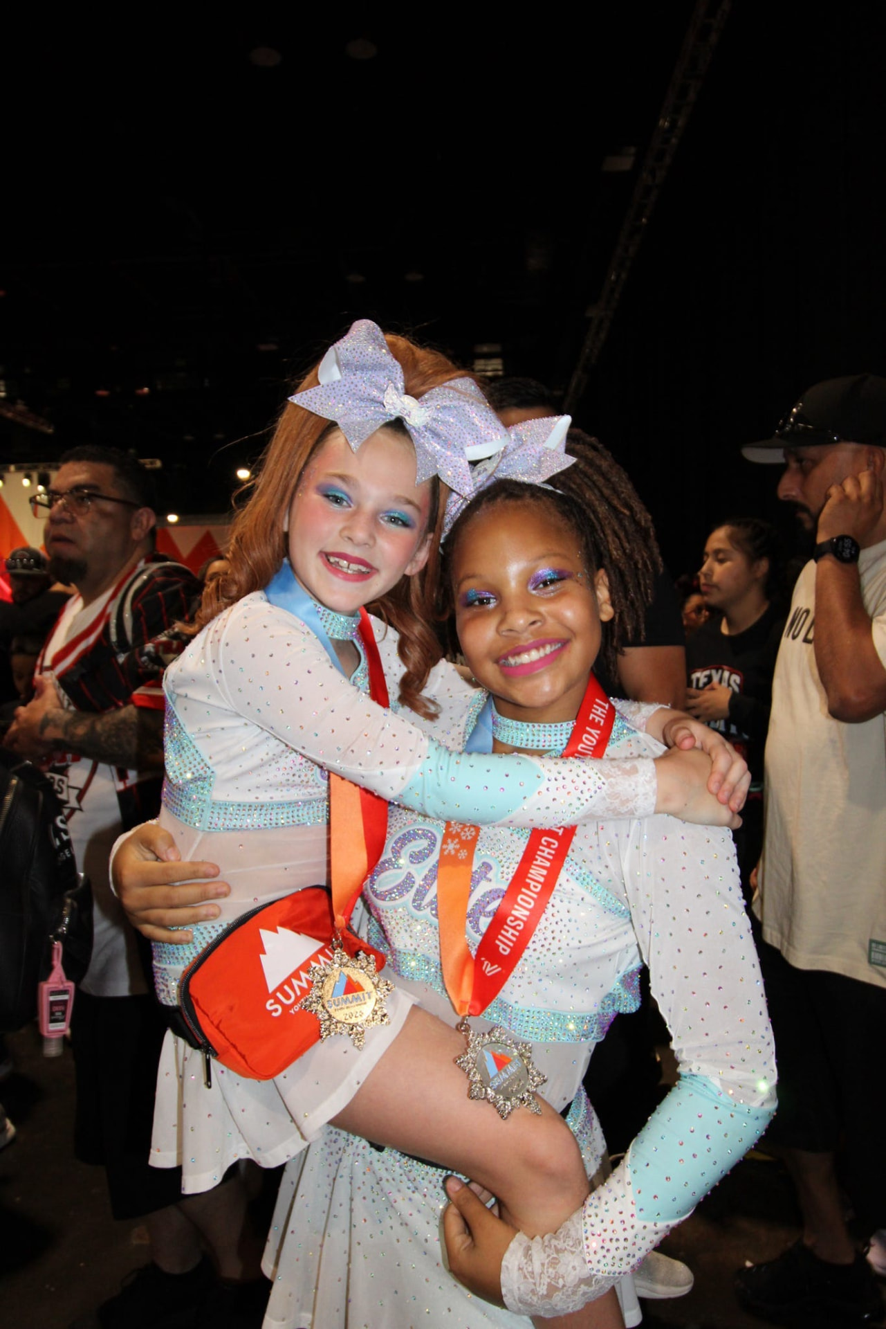 Two smiling Elite Athletics teammates hugging with their Summit medals
