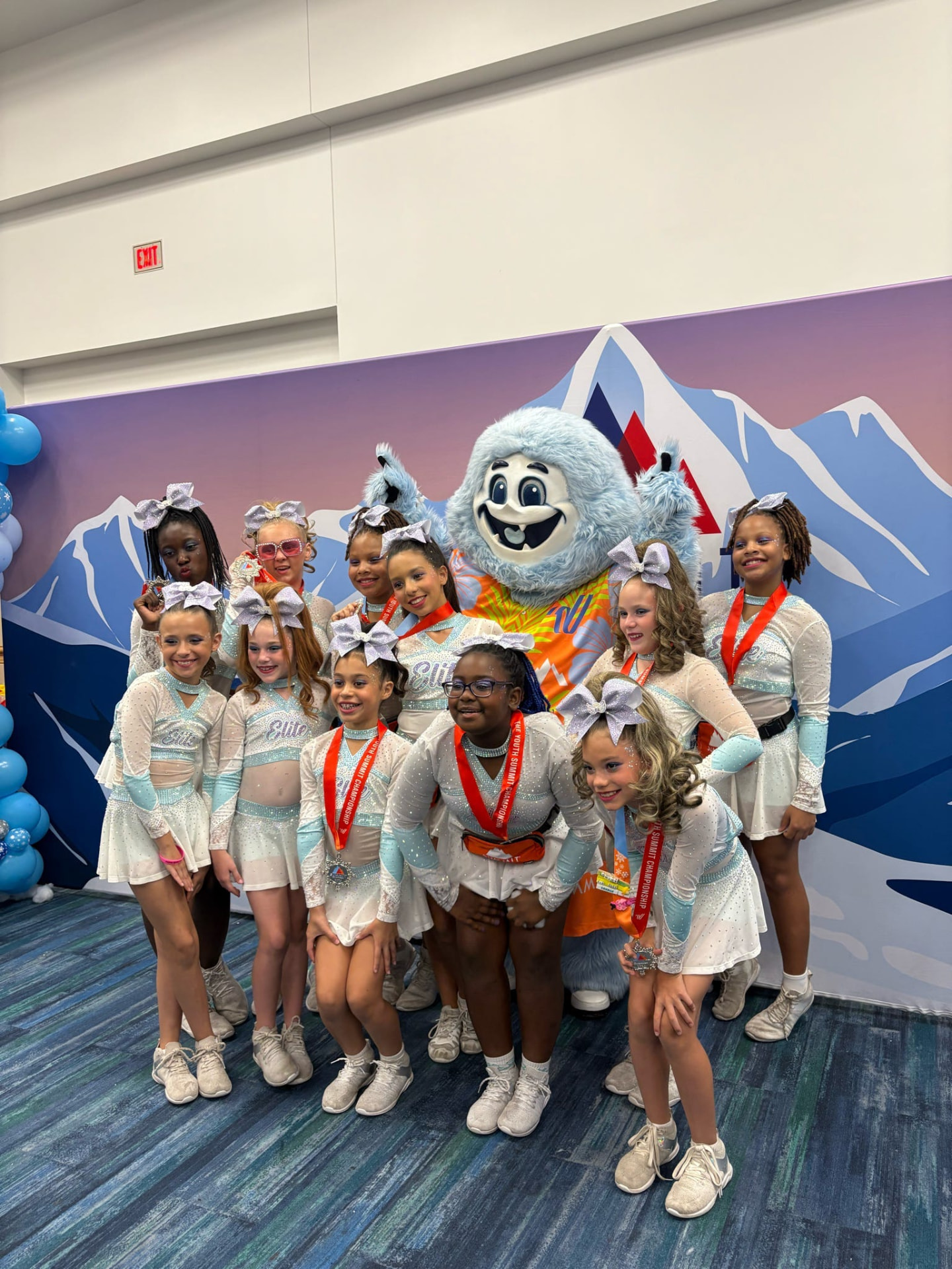Elite Athletics athletes posing together with the Summit mascot and their medals